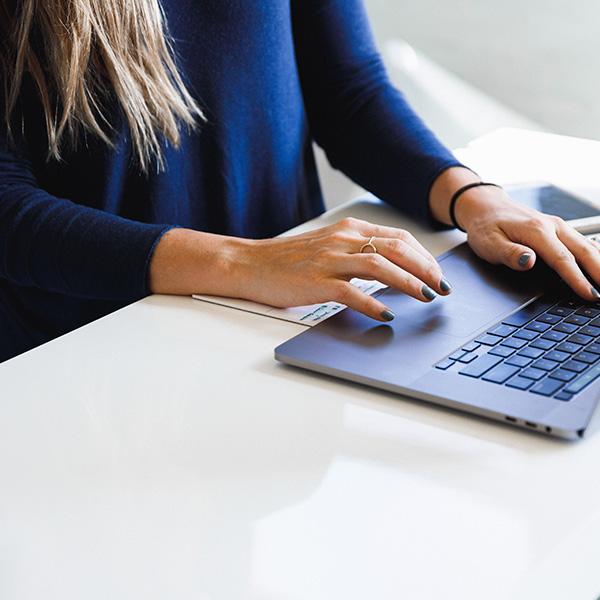 A woman in a dark blue top, working at a desktop on her laptop