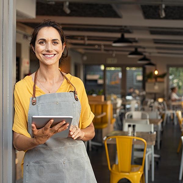 Restaurant owner leaning up against the entrance of her business while holding a tablet