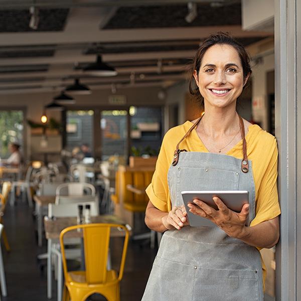 Restaurant owner leaning up against the entrance of her business while holding a tablet